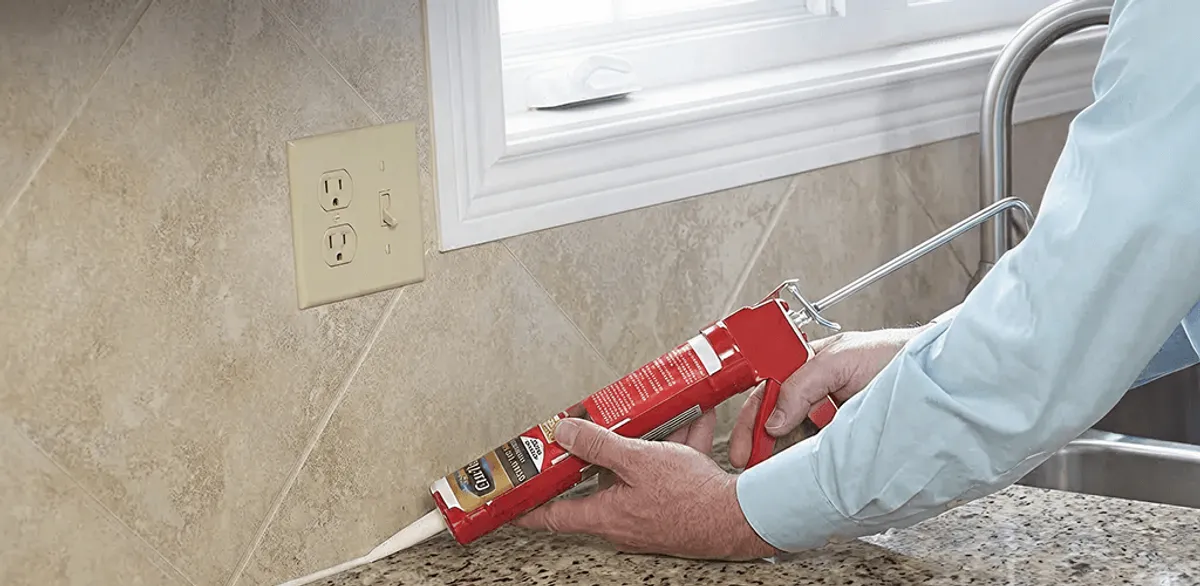 Handyman applying caulk along a kitchen backsplash and countertop seam in Wilmington, NC